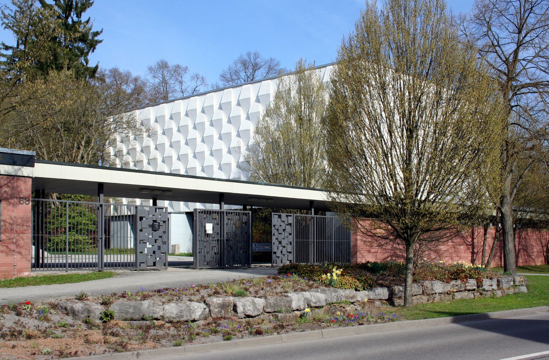 Eingangsbereich mit moderner Feierhalle und markanter weißer Dachfassade auf Friedhof Feuerbach